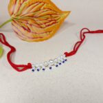 Elegant Pearl Beaded Rakhi with Blue Drops on Red Thread